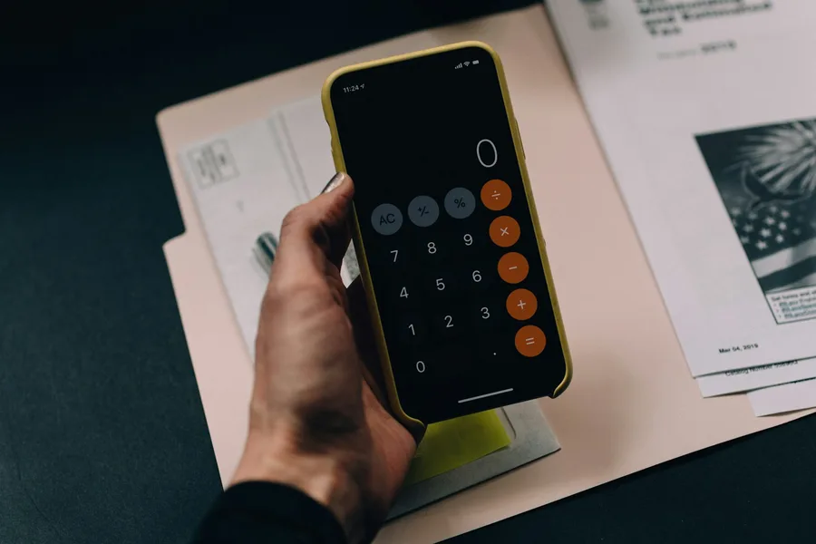 Minimalist dark executive desk with financial workbook and laptop showing automated budgeting calculator